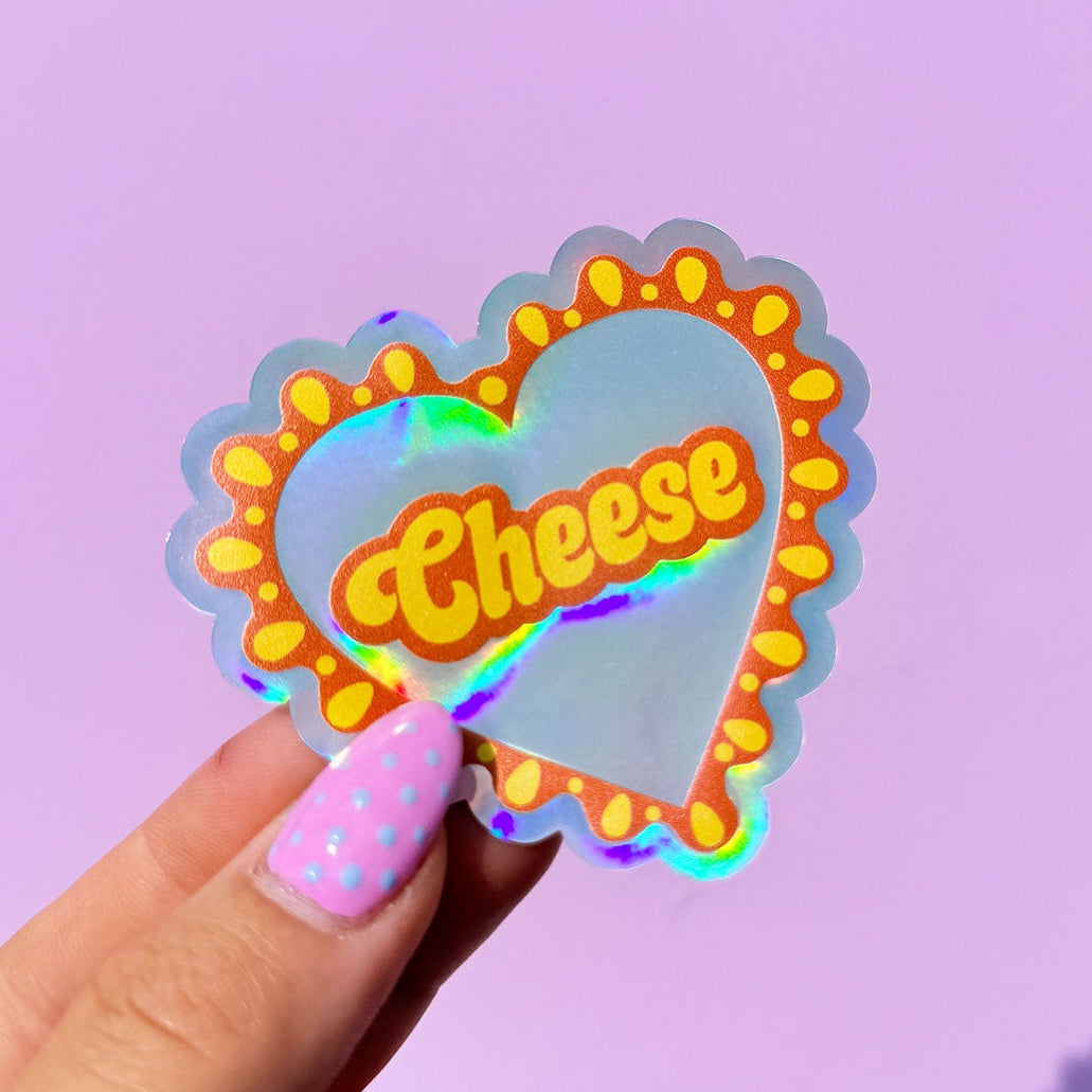 Holographic 'Cheese' sticker held by a hand against a purple background