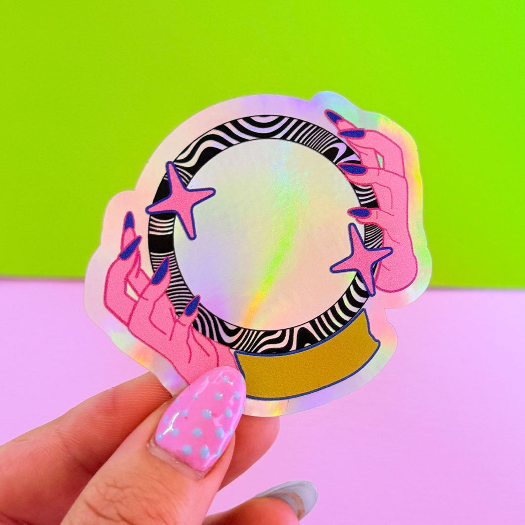 Holographic sticker held by a hand with colorful nail polish against a green and pink gradient background