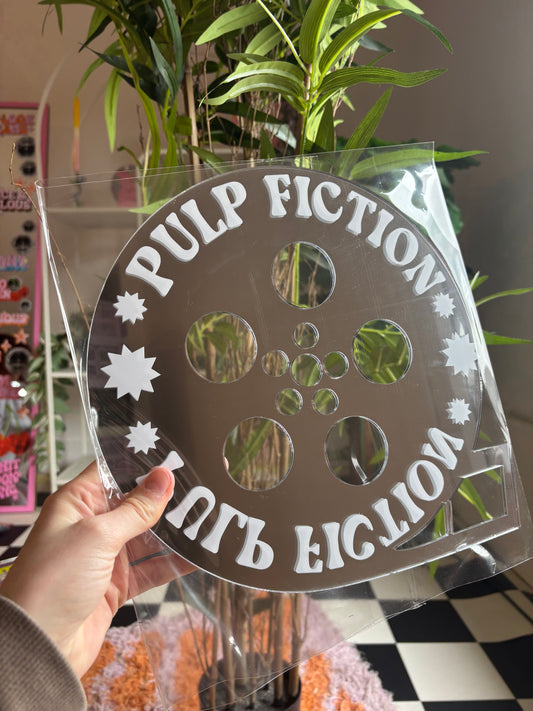A hand is holding a clear plastic object with the text "PULP FICTION" written on it, which appears to be a film reel or projector.