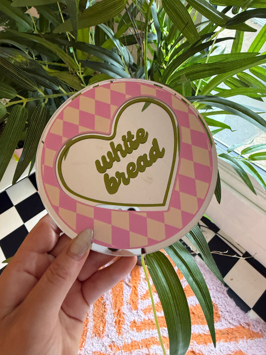 A hand holding a heart-shaped sticker with the text "While I was in the mood for some ice cream" printed on it, surrounded by green leaves and a checkered pattern.