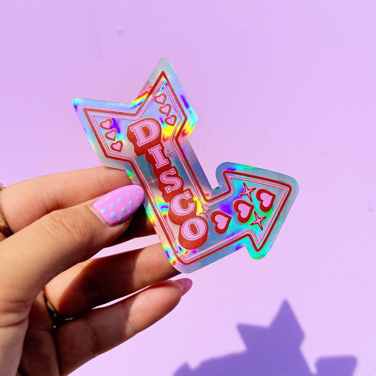 Holographic 'Disco' sticker held by a hand against a purple background