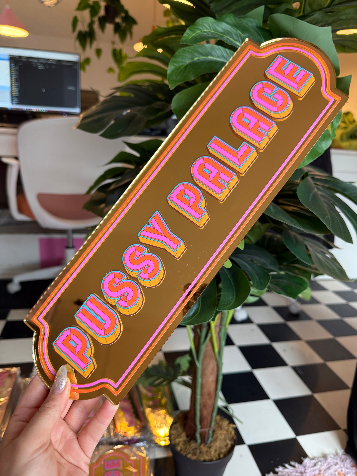 A person is holding a sign with the word "PUSSY" written on it, which is surrounded by various plants and decorative elements.