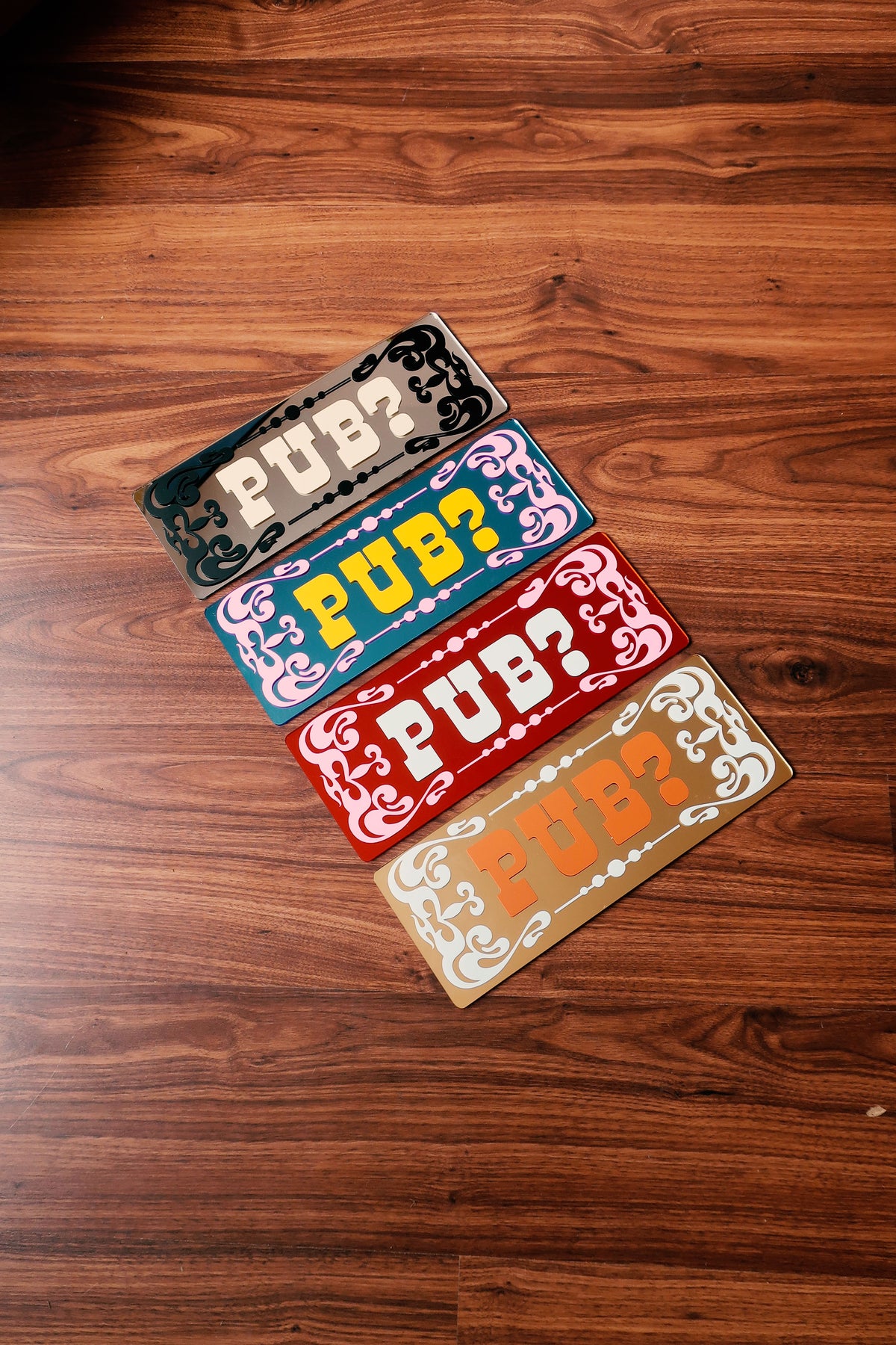 four colorful rectangular signs with the word "PUB?" written on them, placed on a wooden floor.
