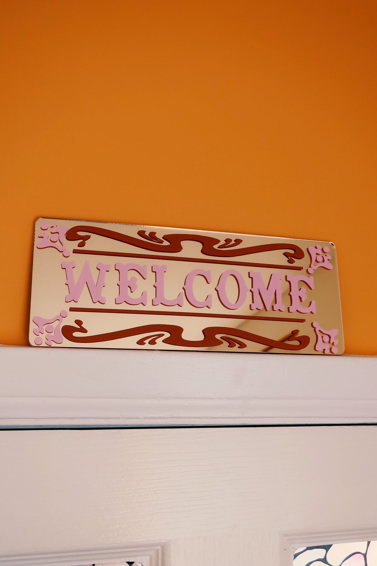 a decorative "Welcome" sign on a wall, with a warm orange background.