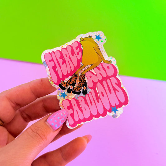 Sticker with a design of a woman in a dress and 'Fierce and Fabulous' text held by a hand against a colorful background.