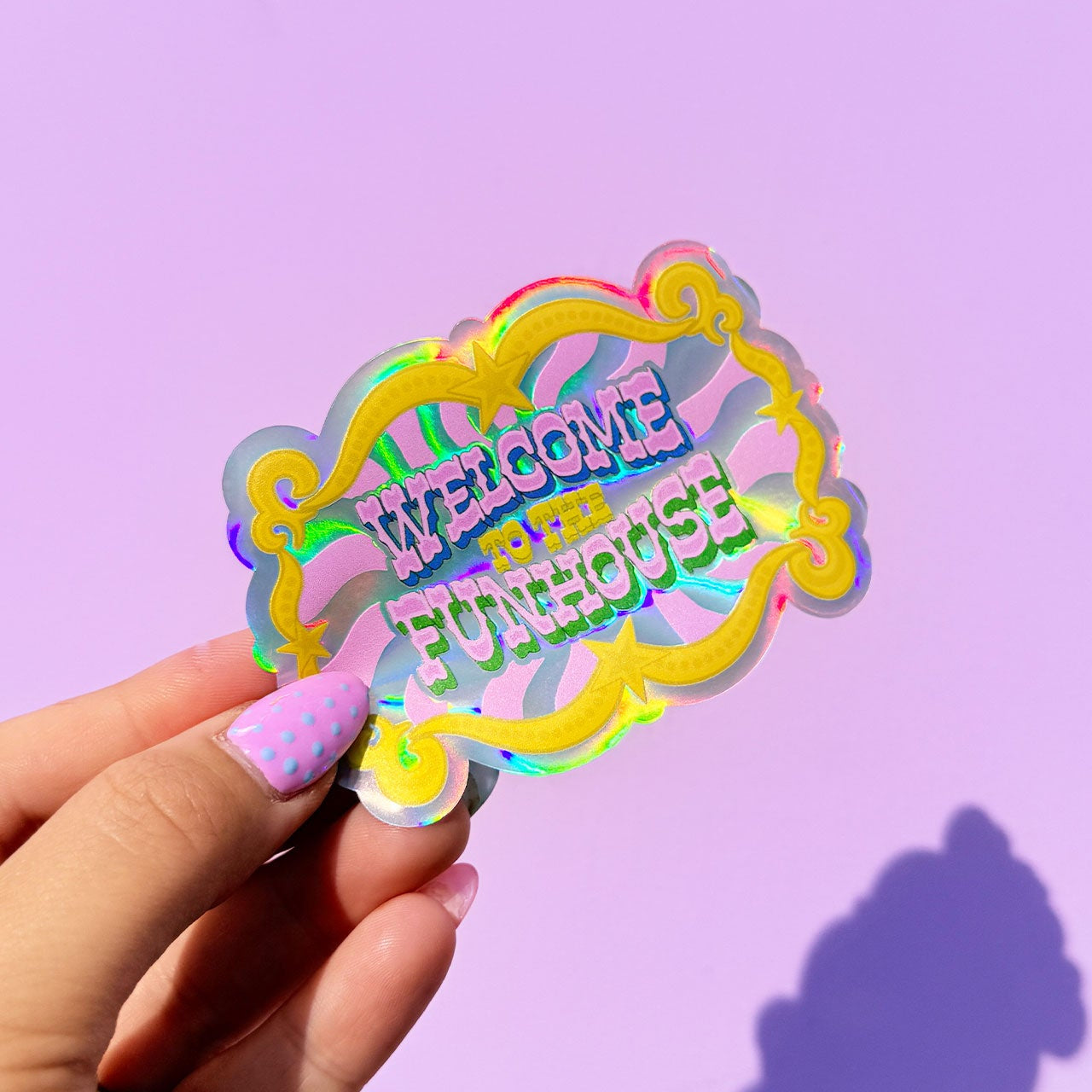 Holographic 'Welcome to the Funhouse' sticker held against a purple background