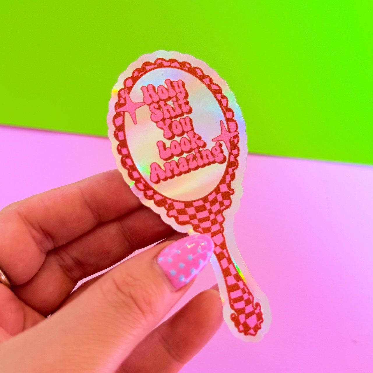 Hand holding a colorful sticker with text against a gradient background