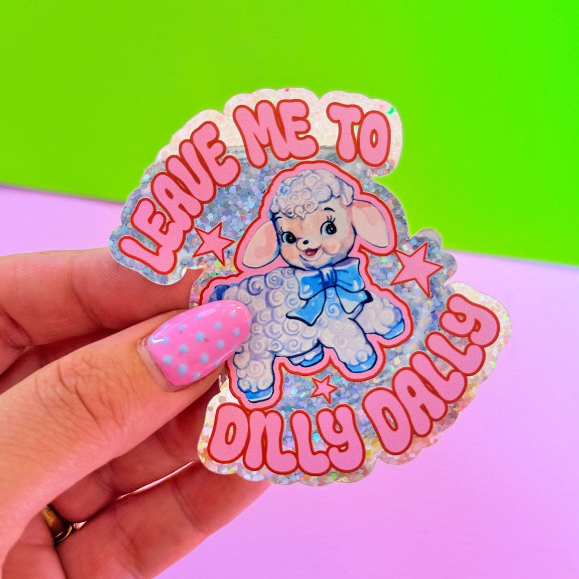 Sticker with cartoon lamb and text held by a hand against a colorful background