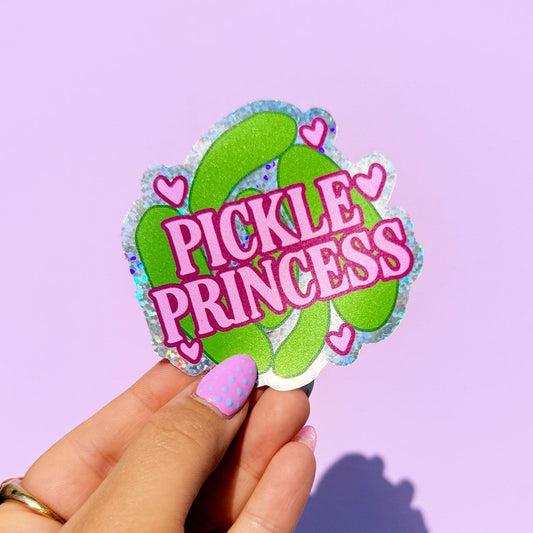 Hand holding a 'Pickle Princess' sticker against a purple background