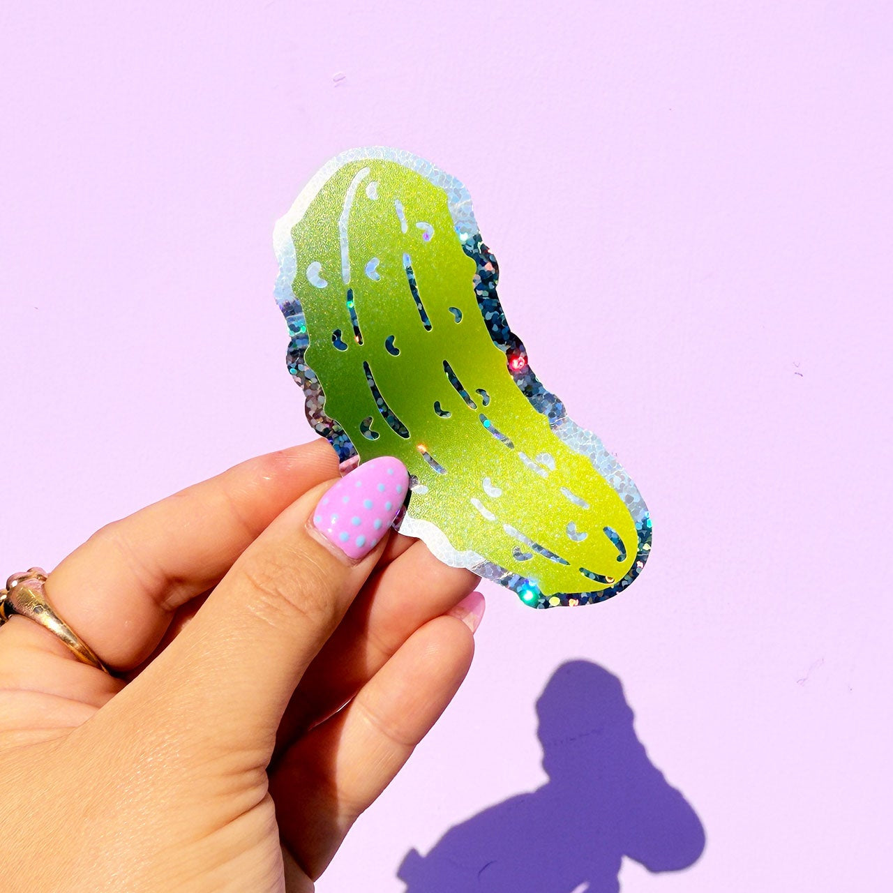 Hand holding a colorful pickle-shaped object against a purple background