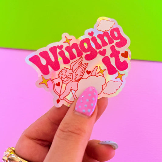 Hand holding a 'Winging it' sticker with a colorful background